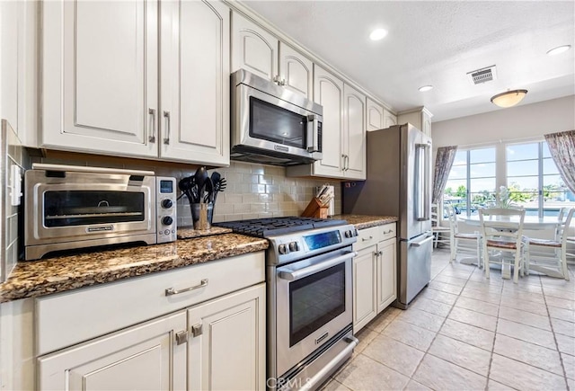 4591 Warner Ave Unit 105, Huntington Beach, CA 92649 - kitchen featuring stainless steel appliances, tasteful backsplash, dark stone countertops, light tile patterned floors, and recessed lighting