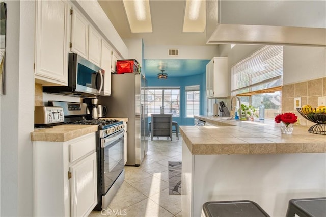 kitchen with appliances with stainless steel finishes, a sink, a peninsula, white cabinetry, and light tile patterned flooring