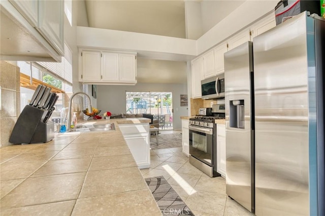 kitchen with appliances with stainless steel finishes, a sink, tile counters, white cabinets, and a high ceiling
