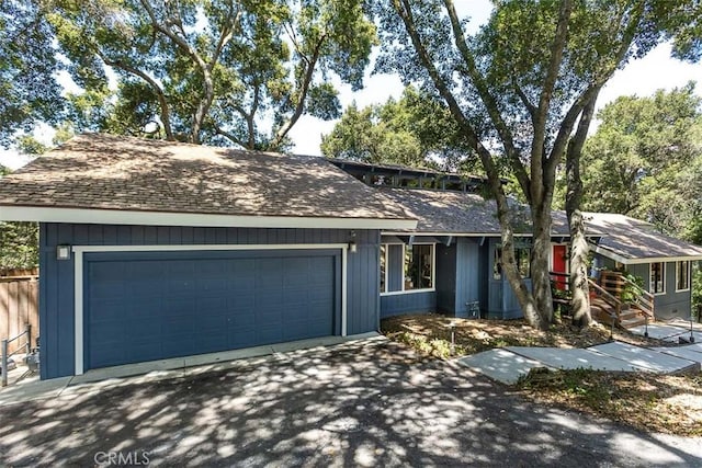view of front of house featuring asphalt driveway, a shingled roof, a garage, and fence