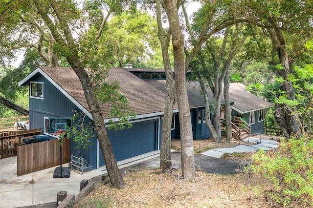 view of front facade with a shingled roof, an attached garage, fence, and driveway