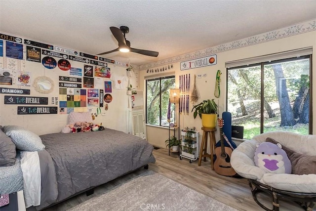 bedroom with wood finished floors, a textured ceiling, multiple windows, and ceiling fan