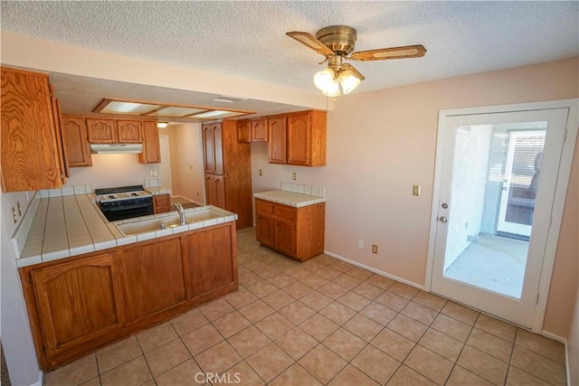 14410 Navajo Rd, Apple Valley, CA 92307 - kitchen with under cabinet range hood, stove, a sink, tile counters, and a peninsula