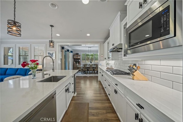 kitchen featuring appliances with stainless steel finishes, a sink, ornamental molding, white cabinetry, and decorative light fixtures
