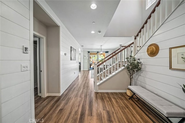 hallway featuring stairway, wooden walls, baseboards, wood finished floors, and recessed lighting