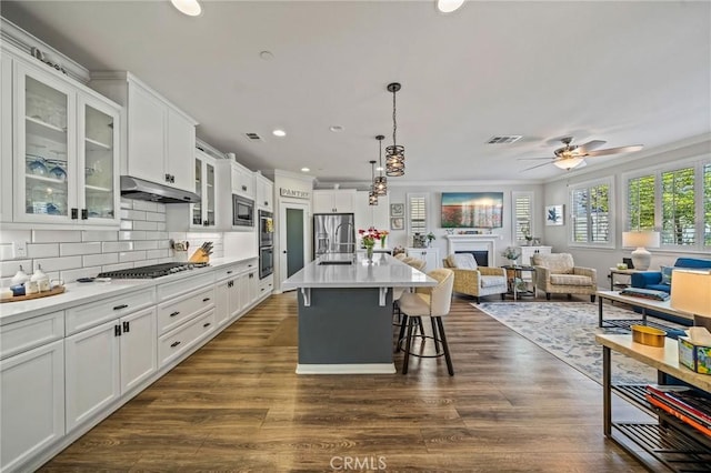 kitchen featuring open floor plan, under cabinet range hood, a kitchen breakfast bar, white cabinetry, and a fireplace