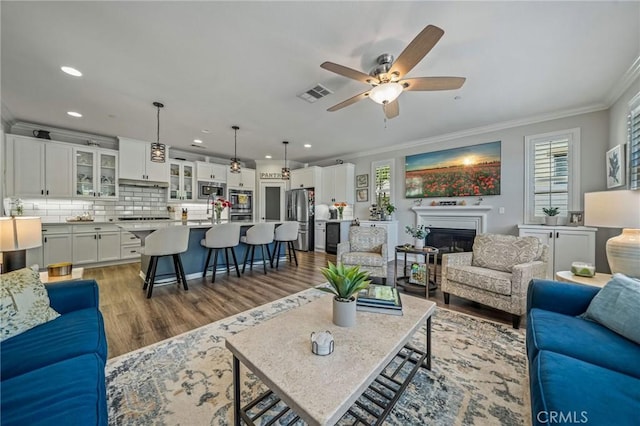 living room featuring ornamental molding, light wood-type flooring, a ceiling fan, recessed lighting, and a glass covered fireplace