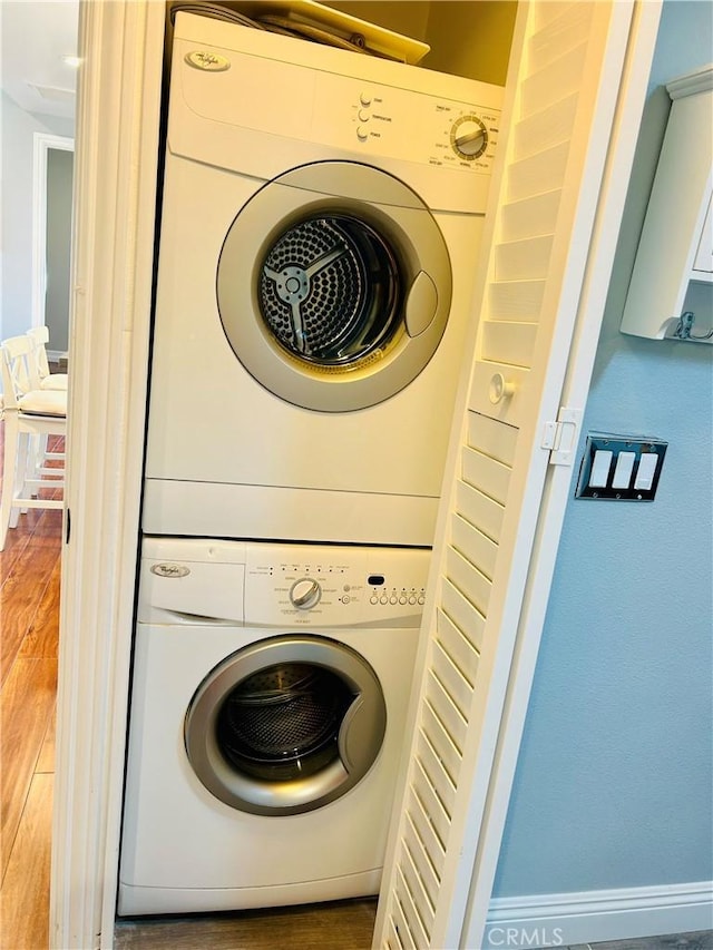 washroom featuring estacked washer and dryer, wood finished floors, and baseboards