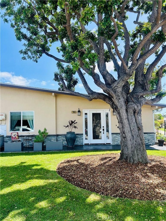view of front facade featuring stucco siding, stone siding, and a front lawn