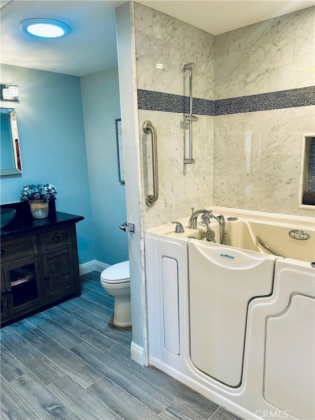 bathroom with a tub to relax in, wood finished floors, vanity, toilet, and baseboards