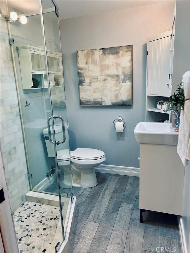 full bathroom featuring wood finished floors, vanity, baseboards, a stall shower, and toilet