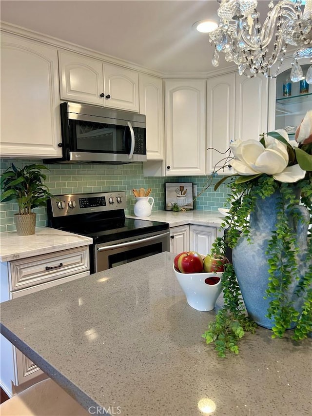 kitchen featuring stainless steel appliances, white cabinetry, light stone counters, decorative backsplash, and a chandelier