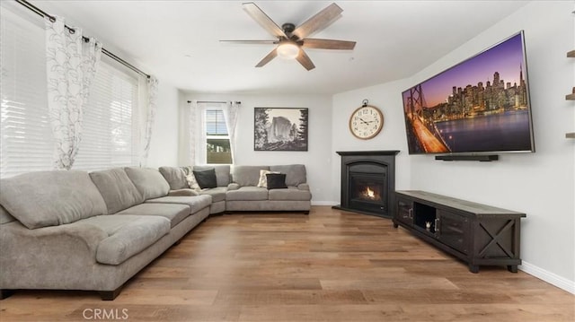 living area with ceiling fan, wood finished floors, baseboards, and a glass covered fireplace