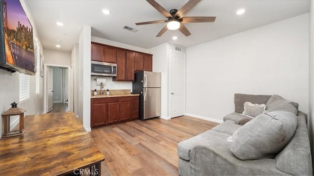 kitchen with stainless steel appliances, open floor plan, a ceiling fan, a sink, and light wood-style floors