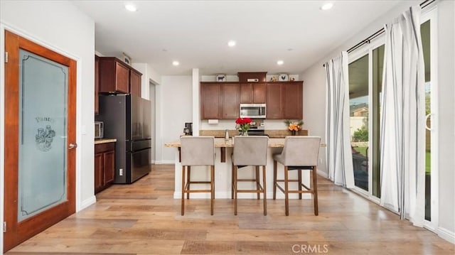 kitchen with appliances with stainless steel finishes, light wood-style floors, a breakfast bar, recessed lighting, and a kitchen island with sink