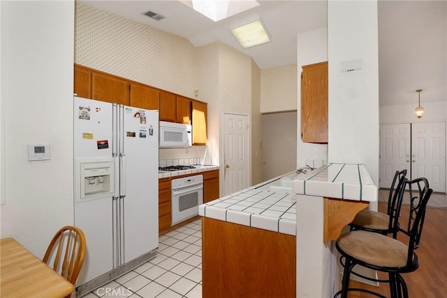 4102 Victoria Ln, Quartz Hill, CA 93536 - kitchen with white appliances, a peninsula, tile counters, brown cabinets, and wallpapered walls