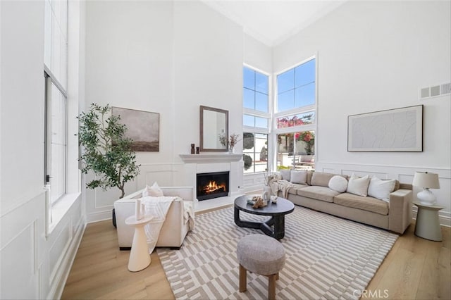 23721 Via Segovia, Murrieta, CA 92562 - living area featuring light wood finished floors, a decorative wall, a warm lit fireplace, a towering ceiling, and a wainscoted wall