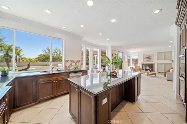 23721 Via Segovia, Murrieta, CA 92562 - kitchen featuring a sink, a glass covered fireplace, a kitchen island, recessed lighting, and crown molding