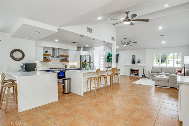 1123 E El Cid E, El Cid, Palm Springs, CA 92262 - kitchen featuring appliances with stainless steel finishes, wall chimney exhaust hood, a kitchen bar, open shelves, and lofted ceiling