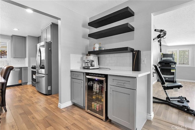 15074 Willow St, Hesperia, CA 92345 - indoor dry bar with wine cooler, stainless steel appliances, a textured ceiling, decorative backsplash, and light wood-style flooring