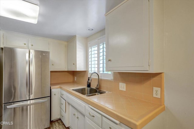 kitchen with freestanding refrigerator, a sink, tile countertops, and white cabinetry