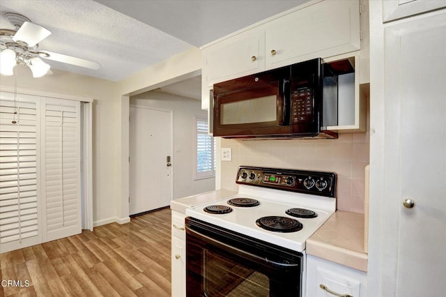 kitchen featuring electric range, black microwave, tile countertops, decorative backsplash, and white cabinets