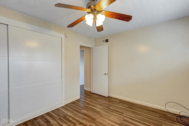 unfurnished bedroom with wood finished floors, baseboards, a closet, a textured ceiling, and a ceiling fan