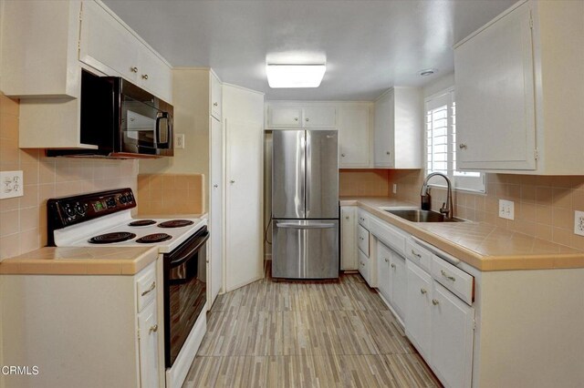 kitchen with freestanding refrigerator, white electric range oven, a sink, black microwave, and tile countertops