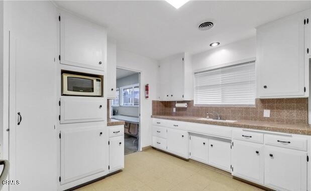 kitchen with white microwave, a sink, white cabinetry, and tasteful backsplash