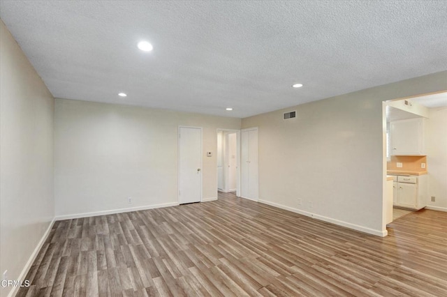 spare room featuring light wood-style flooring, recessed lighting, baseboards, and a textured ceiling