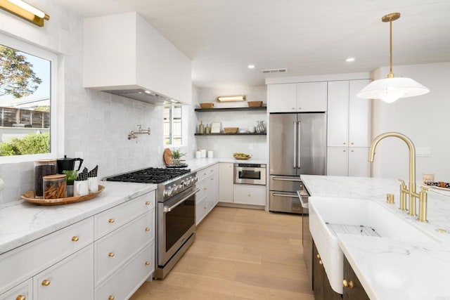 kitchen with high quality appliances, light wood-type flooring, tasteful backsplash, custom exhaust hood, and white cabinetry