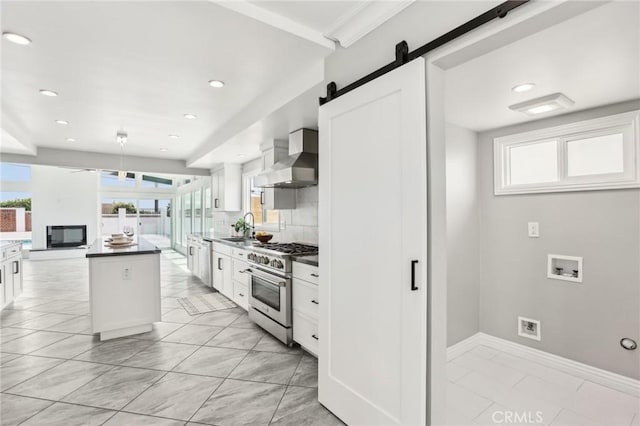 kitchen with appliances with stainless steel finishes, wall chimney exhaust hood, a sink, white cabinets, and a barn door