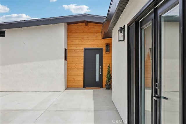 doorway to property featuring elevator, stucco siding, and a patio