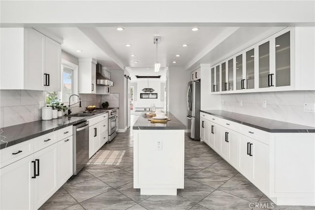 kitchen featuring stainless steel appliances, a sink, wall chimney range hood, a center island, and light marble finish floors
