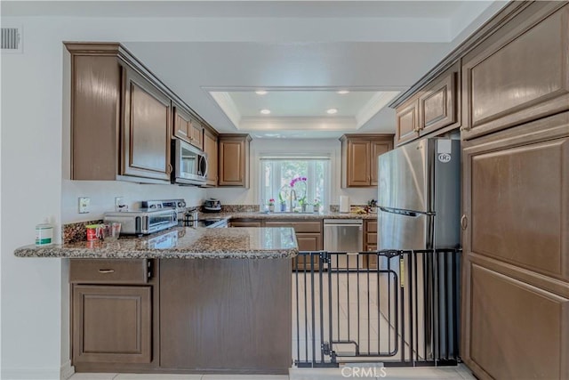 5855 Via Sonora Unit 39, Yorba Linda, CA 92887 - kitchen with appliances with stainless steel finishes, a tray ceiling, light stone countertops, a peninsula, and a sink