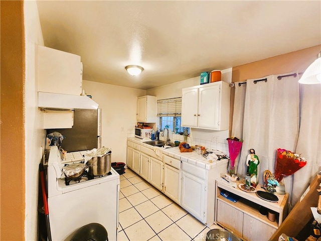 1210 W Manchester Ave, Los Angeles, CA 90044 - kitchen featuring tile counters, washer / dryer, a sink, light tile patterned floors, and white cabinets