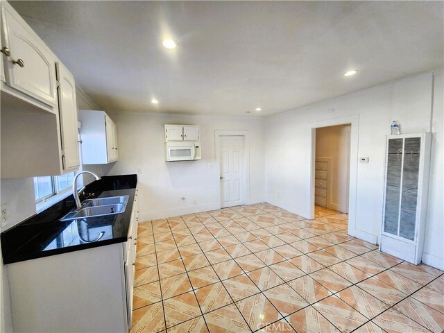 1210 W Manchester Ave, Los Angeles, CA 90044 - kitchen with white microwave, a heating unit, dark countertops, a sink, and white cabinetry