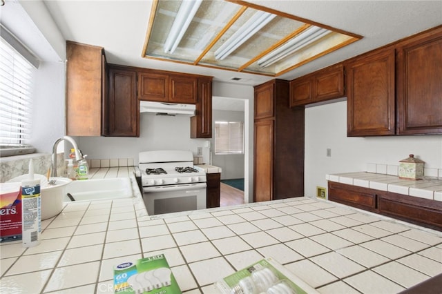 kitchen featuring gas range gas stove, under cabinet range hood, a sink, and tile counters