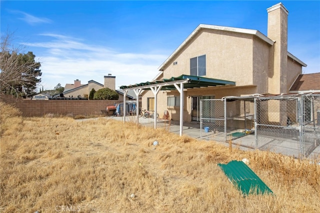 rear view of house with a patio area, stucco siding, fence, and a chimney