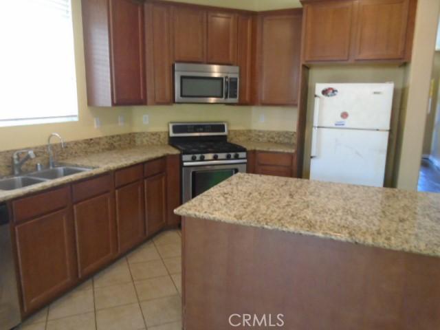 29221 Loden Cir, Menifee, CA 92584 - kitchen with appliances with stainless steel finishes, a sink, light stone counters, light tile patterned floors, and brown cabinetry