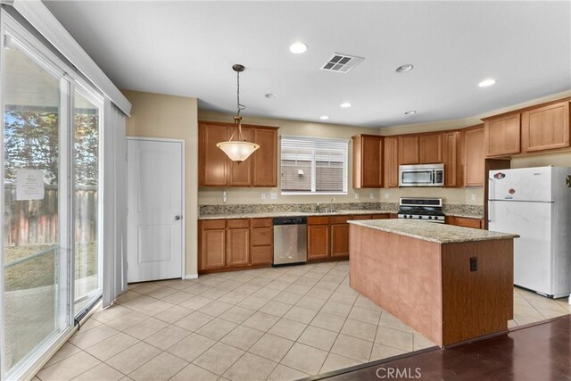 29221 Loden Cir, Menifee, CA 92584 - kitchen with appliances with stainless steel finishes, a center island, brown cabinetry, decorative light fixtures, and light stone counters