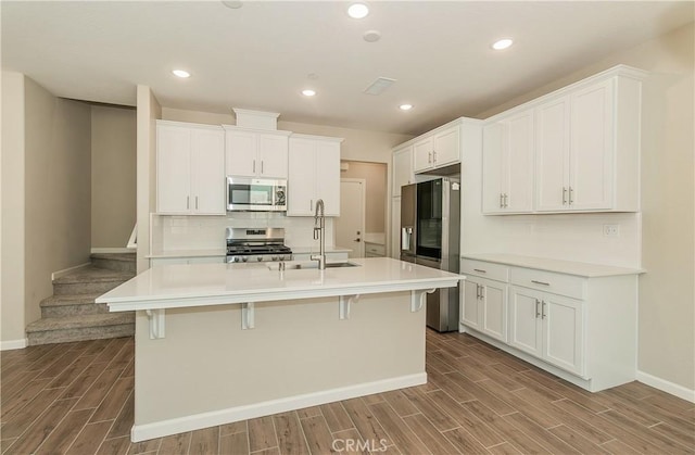 1123 Vanguard Way W, Madera, CA 93636 - kitchen with appliances with stainless steel finishes, a sink, wood tiled floors, baseboards, and an island with sink