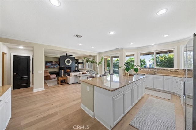 46397 Kohinoor Way, Temecula, CA 92592 - kitchen with a center island, white cabinetry, ornamental molding, light stone counters, and light wood-style floors
