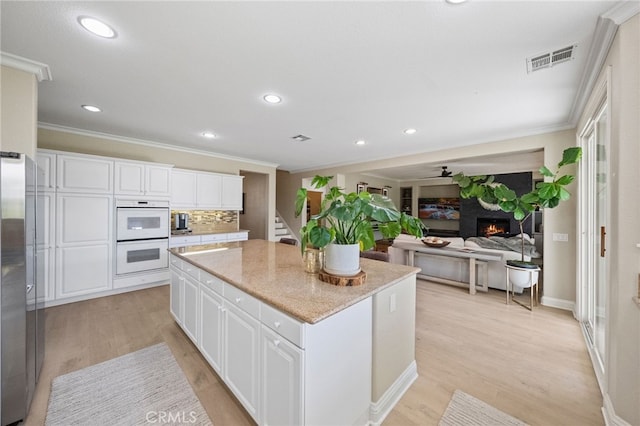 46397 Kohinoor Way, Temecula, CA 92592 - kitchen featuring white double oven, crown molding, a center island, a lit fireplace, and light wood finished floors