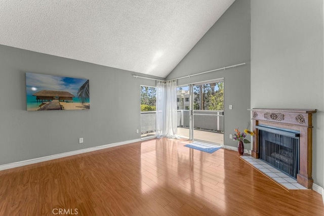 628 Daisy Ave Unit 420, Long Beach, CA 90802 - unfurnished living room with wood finished floors, a tiled fireplace, a textured ceiling, baseboards, and high vaulted ceiling