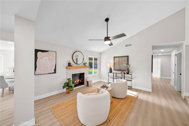 living room with light wood-style flooring, ceiling fan, a tiled fireplace, baseboards, and high vaulted ceiling