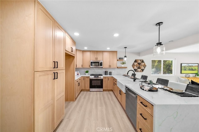kitchen with appliances with stainless steel finishes, light brown cabinetry, a sink, a peninsula, and light wood finished floors