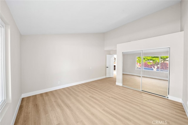 unfurnished bedroom with lofted ceiling, light wood finished floors, baseboards, and a closet