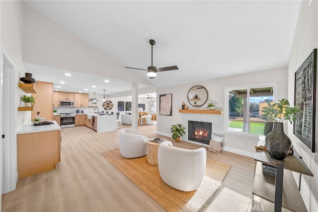 living area featuring a warm lit fireplace, light wood finished floors, ceiling fan, vaulted ceiling, and recessed lighting