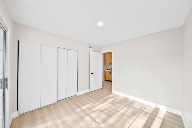 unfurnished bedroom featuring baseboards, light wood-style flooring, a closet, and recessed lighting